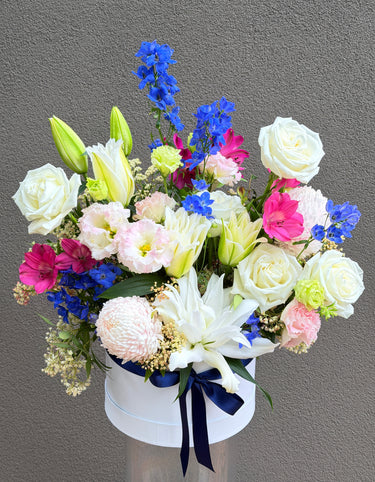 flowers arranged in a white hatbox with a grey background