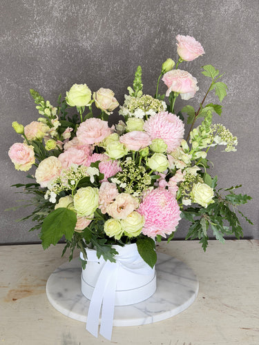 pink and green flowers arrangement in a white hat box against a dark wall designed in Mount Waverley